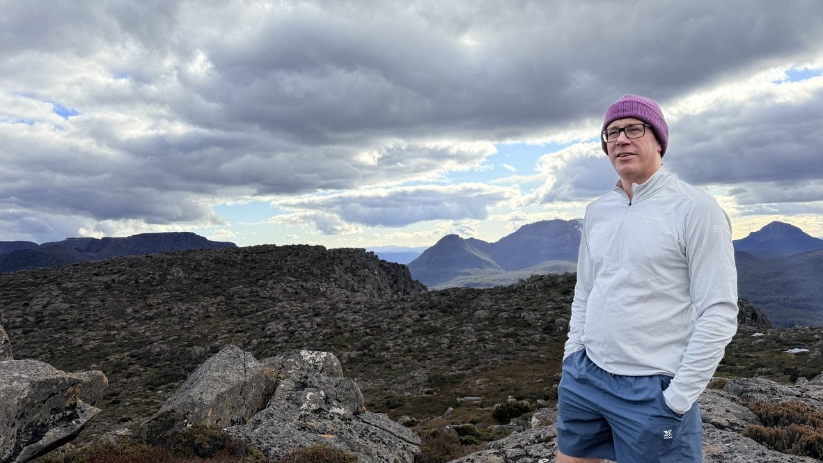 Mowser standing on a granite summit with Tasmanian mountains behind him
